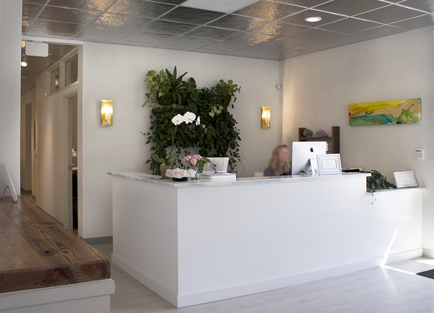 The white reception area a green “living” wall sits behind the desk, warm amber sconces border the plants